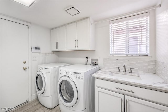 laundry room with a sink, visible vents, cabinet space, light wood finished floors, and washer and clothes dryer