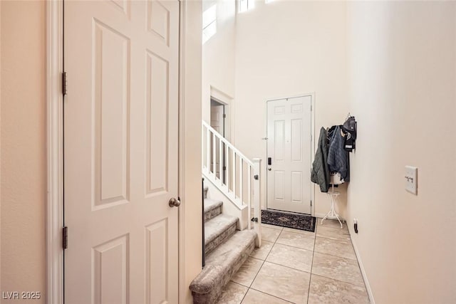 foyer featuring a towering ceiling, baseboards, stairway, and light tile patterned flooring