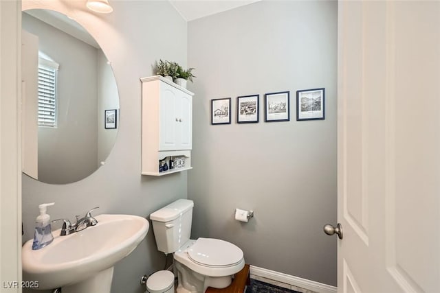 half bathroom with toilet, baseboards, and a sink