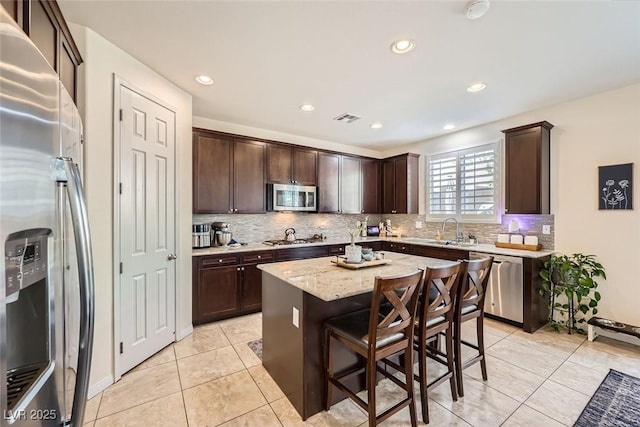 kitchen with visible vents, appliances with stainless steel finishes, a sink, a kitchen island, and dark brown cabinets