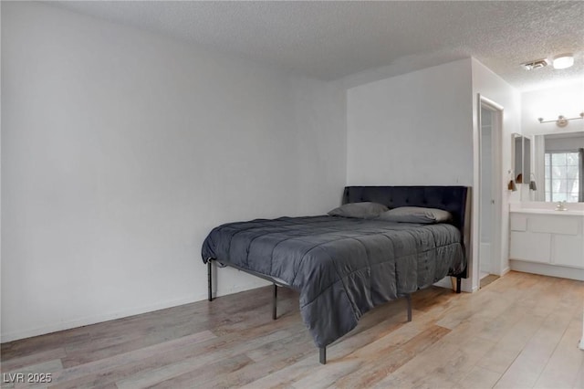 bedroom featuring visible vents, connected bathroom, a textured ceiling, and wood finished floors