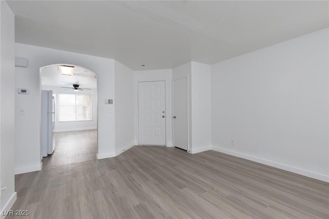 unfurnished room with baseboards, arched walkways, wood finished floors, and a ceiling fan