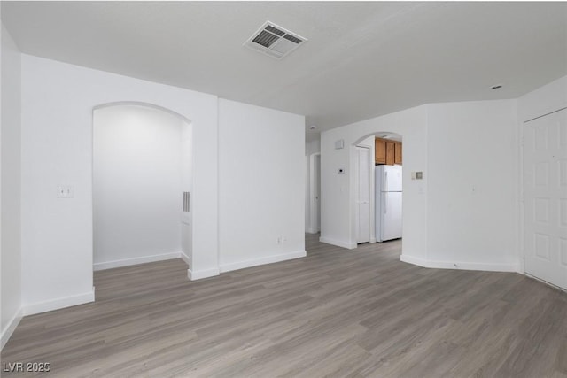 spare room featuring arched walkways, visible vents, baseboards, and light wood-style floors