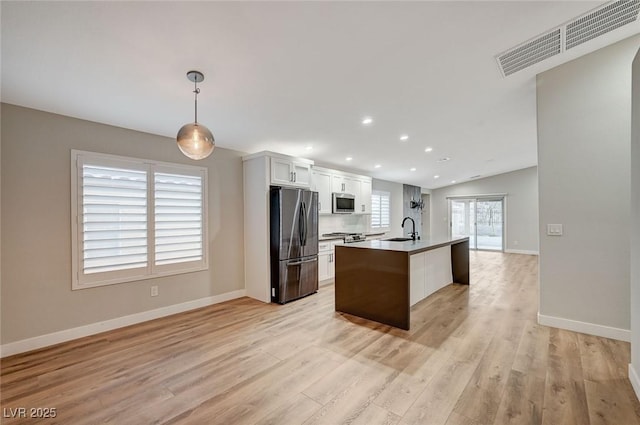 kitchen featuring stainless steel microwave, visible vents, freestanding refrigerator, a sink, and light wood-type flooring