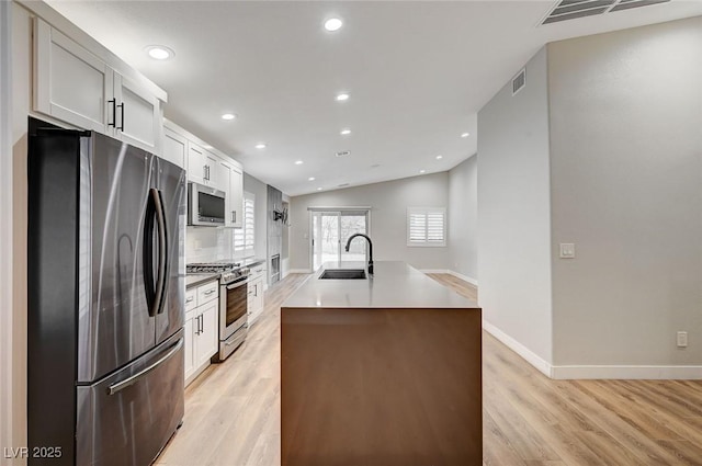 kitchen featuring visible vents, appliances with stainless steel finishes, a kitchen island with sink, a sink, and light wood-type flooring