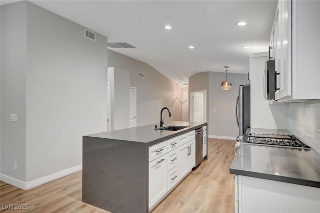 kitchen with stainless steel appliances, dark countertops, a sink, and a center island with sink