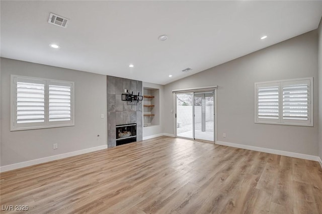 unfurnished living room with baseboards, visible vents, a tiled fireplace, lofted ceiling, and light wood-type flooring