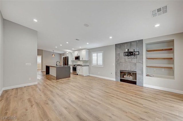 unfurnished living room with light wood-type flooring, baseboards, a fireplace, and visible vents