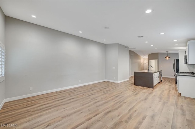 kitchen with a kitchen island with sink, recessed lighting, a sink, open floor plan, and light wood-type flooring