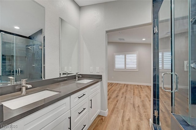 full bath with double vanity, wood finished floors, a stall shower, and a sink