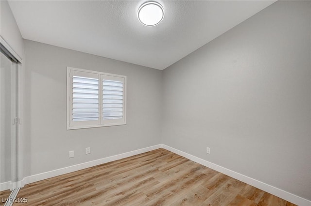 empty room featuring light wood finished floors, baseboards, and a textured ceiling