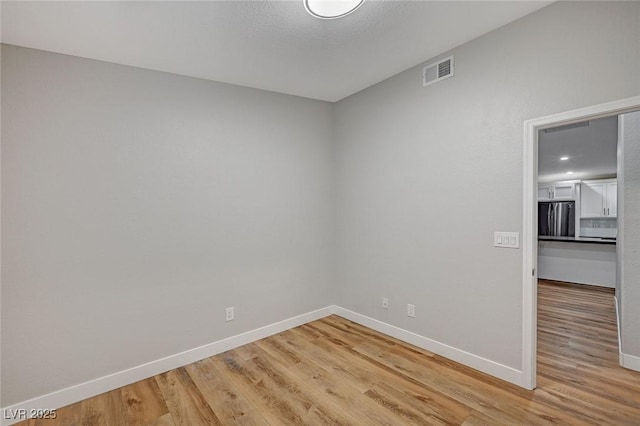 empty room featuring light wood-type flooring, visible vents, and baseboards