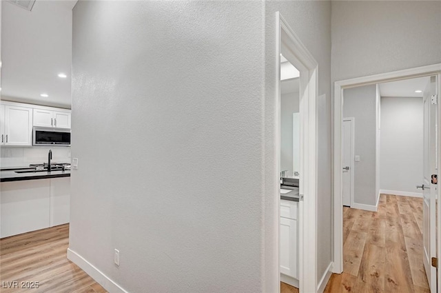 corridor featuring light wood-style flooring, baseboards, and recessed lighting