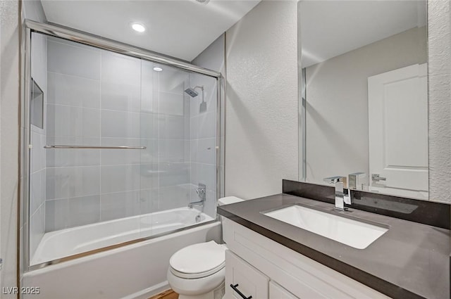 bathroom with a textured wall, combined bath / shower with glass door, vanity, and toilet