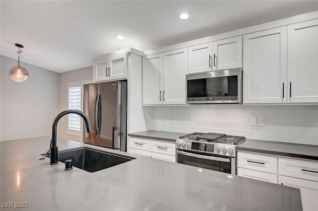 kitchen with a sink, white cabinets, hanging light fixtures, appliances with stainless steel finishes, and dark countertops