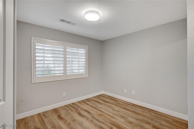 unfurnished room featuring a textured ceiling, wood finished floors, visible vents, and baseboards