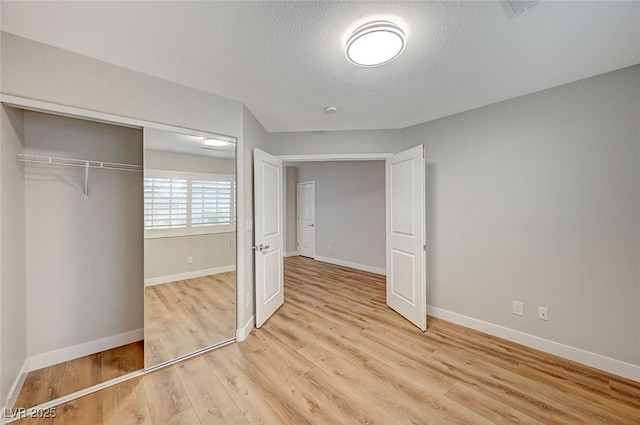 unfurnished bedroom with a textured ceiling, light wood finished floors, a closet, and baseboards