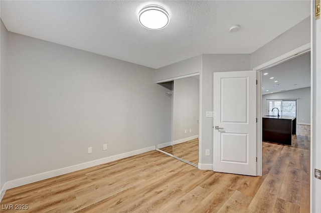 unfurnished bedroom with light wood-style floors, a closet, a textured ceiling, and baseboards