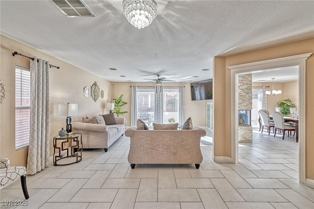 living area with ceiling fan with notable chandelier, a textured ceiling, visible vents, and baseboards