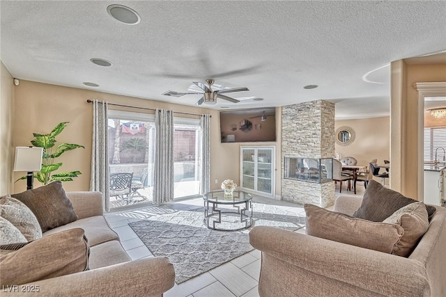 living area featuring ceiling fan, a stone fireplace, and a textured ceiling