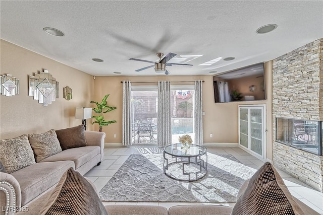 living area with a textured ceiling, light tile patterned flooring, a ceiling fan, and baseboards