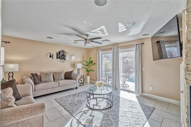 living room featuring a ceiling fan, baseboards, visible vents, and a textured ceiling