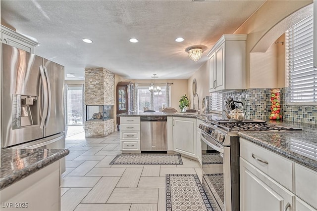 kitchen with a textured ceiling, a notable chandelier, stainless steel appliances, a peninsula, and tasteful backsplash