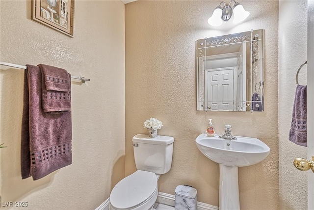 bathroom featuring baseboards, a textured wall, and toilet