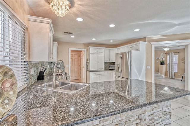 kitchen featuring visible vents, stainless steel fridge with ice dispenser, a peninsula, a sink, and backsplash