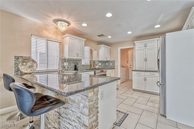 kitchen featuring a peninsula, a sink, white cabinetry, freestanding refrigerator, and washer and clothes dryer