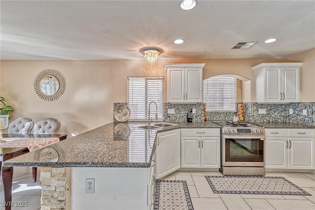 kitchen with visible vents, a peninsula, stainless steel gas range, white cabinetry, and a sink