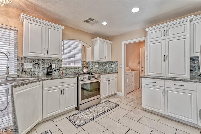 kitchen featuring washer and clothes dryer, visible vents, stainless steel gas stove, a sink, and white cabinetry