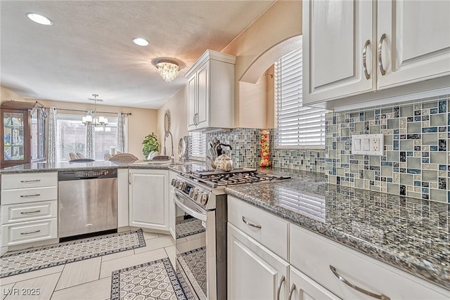 kitchen featuring light tile patterned floors, backsplash, appliances with stainless steel finishes, white cabinets, and a peninsula