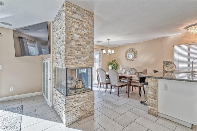 kitchen with a fireplace, visible vents, dark stone countertops, a chandelier, and baseboards