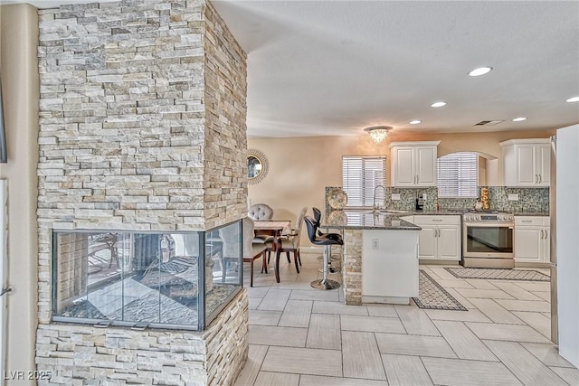 kitchen featuring tasteful backsplash, a peninsula, stainless steel gas range, white cabinetry, and a sink