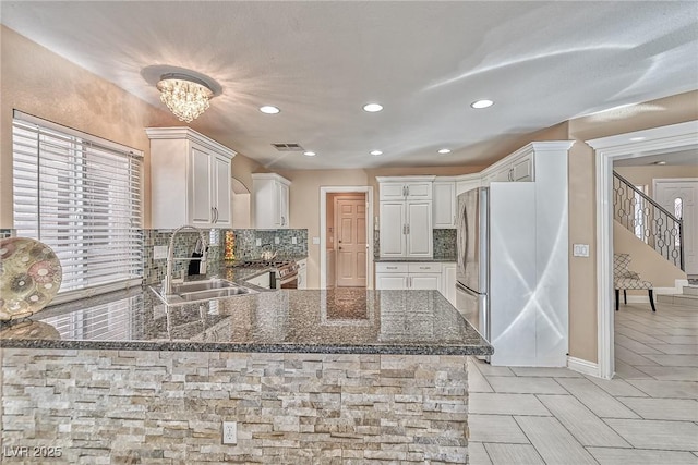 kitchen featuring a peninsula, a sink, appliances with stainless steel finishes, decorative backsplash, and dark stone countertops