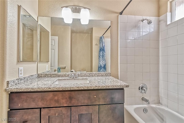 full bathroom featuring shower / bath combo, a textured wall, and vanity