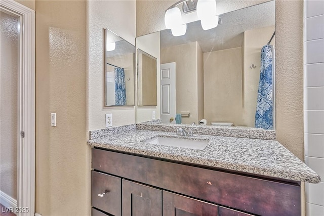 full bathroom with a textured wall, vanity, and a shower with curtain