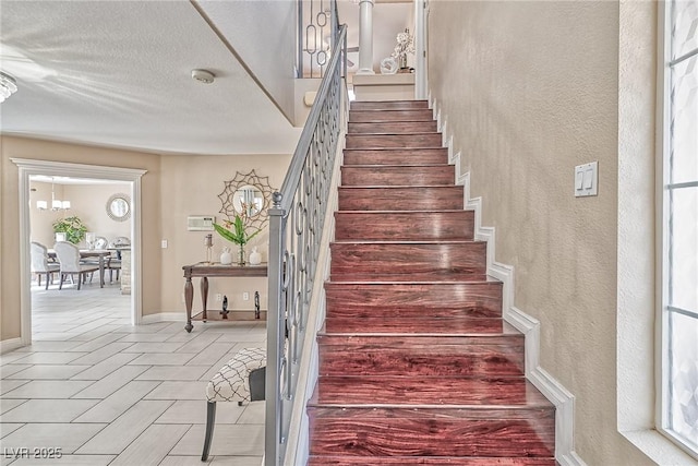 stairs with a textured wall, tile patterned flooring, a notable chandelier, and a textured ceiling