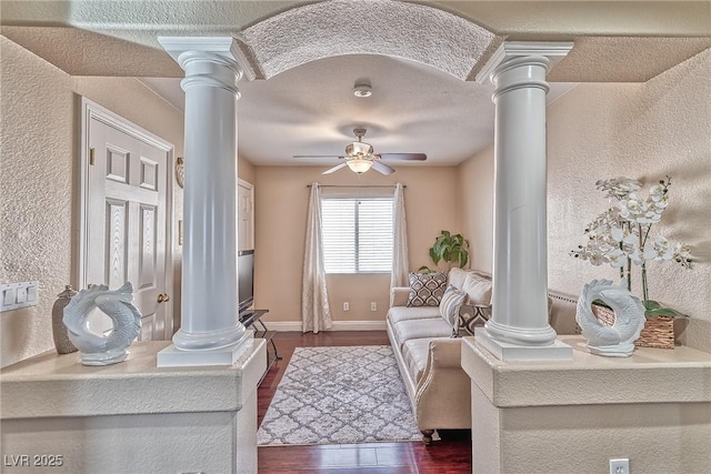 living area featuring decorative columns, ceiling fan, and dark wood-type flooring