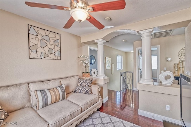 living room featuring arched walkways, visible vents, ornate columns, and wood finished floors