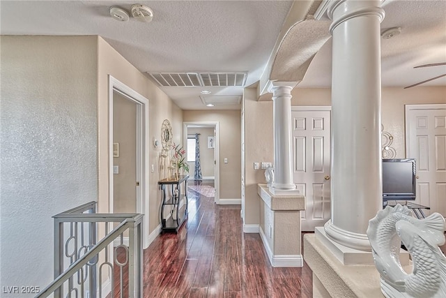 hallway featuring dark wood-style floors, decorative columns, visible vents, a textured ceiling, and baseboards