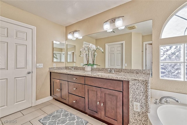 bathroom featuring a bath, double vanity, a sink, and visible vents