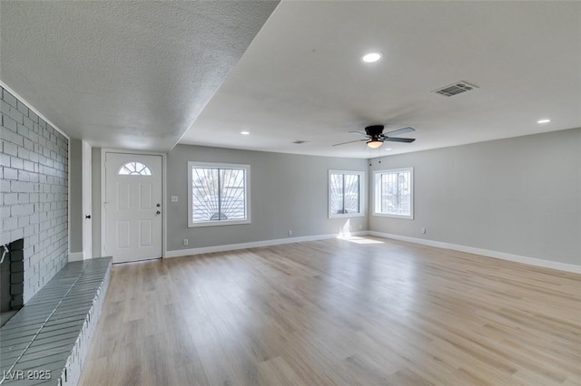 entrance foyer with visible vents, baseboards, light wood-style flooring, a fireplace, and a textured ceiling