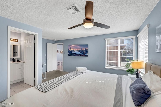 bedroom with visible vents, ensuite bathroom, a textured ceiling, and tile patterned floors