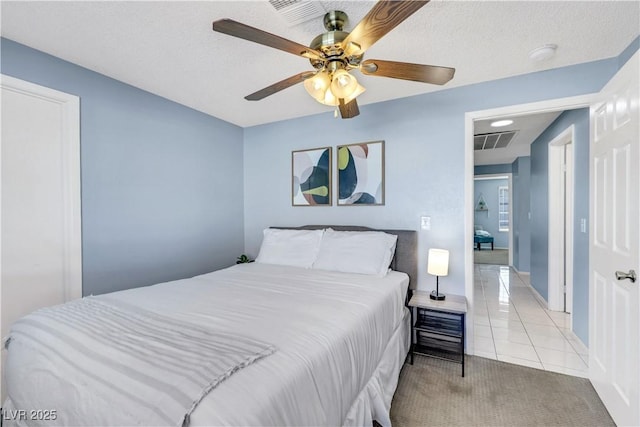 bedroom featuring light tile patterned floors, ceiling fan, a textured ceiling, light carpet, and visible vents