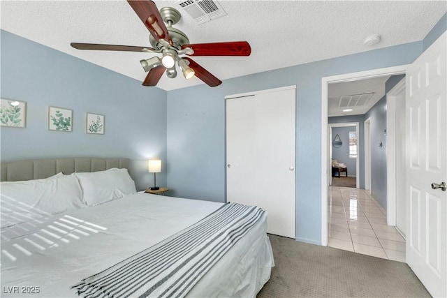 bedroom with light tile patterned floors, visible vents, a closet, and light colored carpet