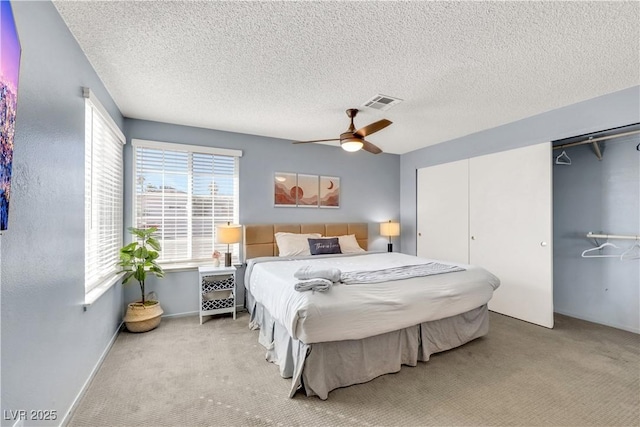 carpeted bedroom with ceiling fan, a textured ceiling, visible vents, baseboards, and a closet