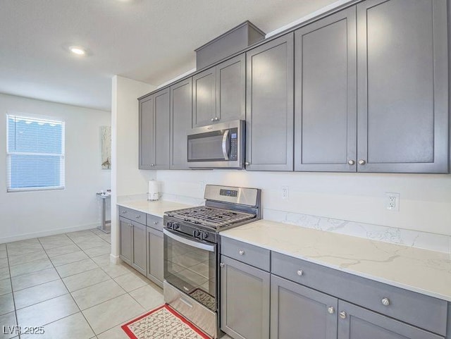 kitchen featuring gray cabinetry, baseboards, light stone countertops, light tile patterned floors, and appliances with stainless steel finishes