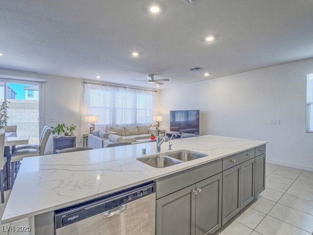 kitchen featuring visible vents, gray cabinetry, a sink, stainless steel dishwasher, and open floor plan